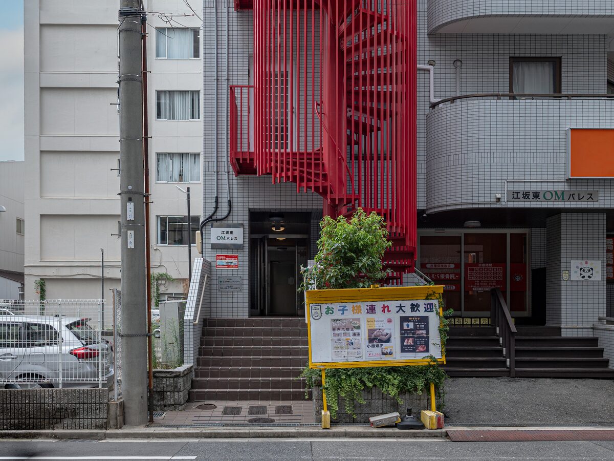 江坂東OMパレスの外観。赤い螺旋階段が目印で、右手に建物名の看板、中央の階段を上がったところが入口